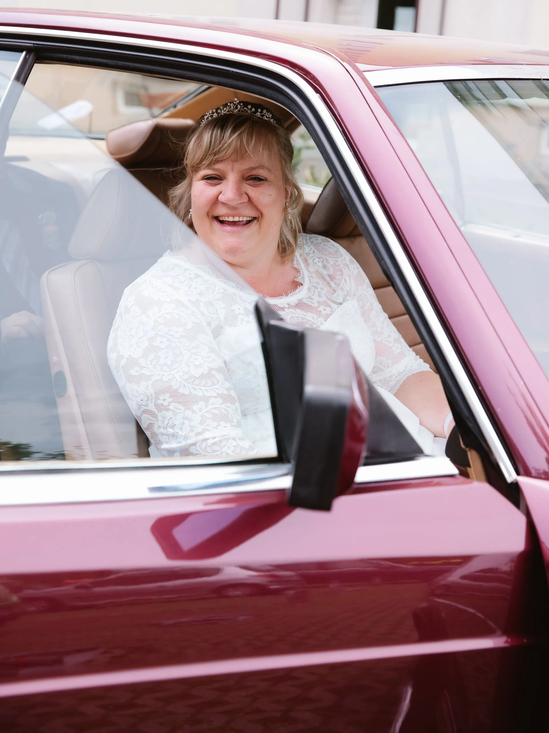 Strahlende Braut lacht aus einem roten Oldtimer